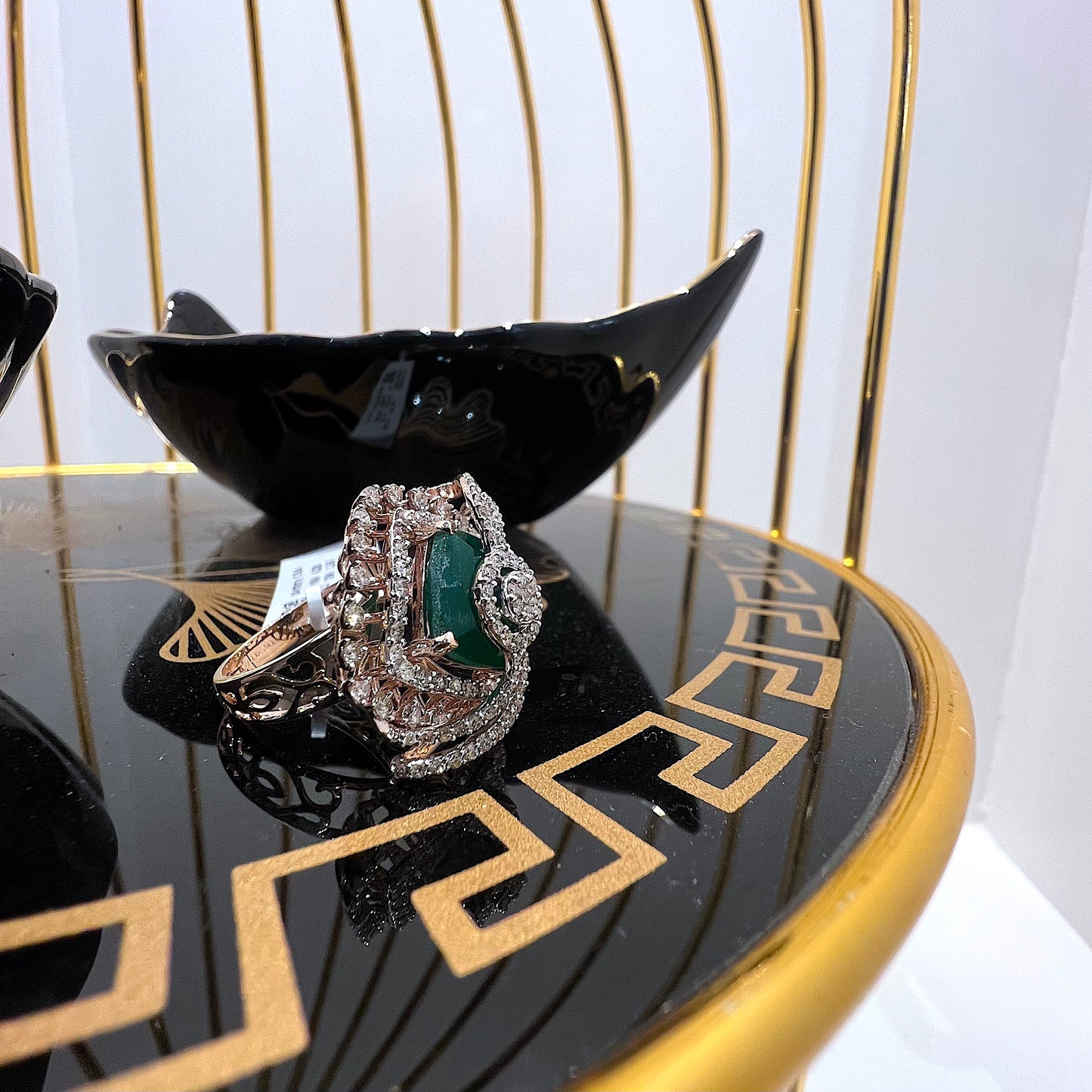A handcrafted natural diamond solid gold ring with a green gemstone and intricate gold detailing, displayed on a black reflective surface.