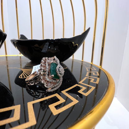 A handcrafted natural diamond solid gold ring with a green gemstone and intricate gold detailing, displayed on a black reflective surface.