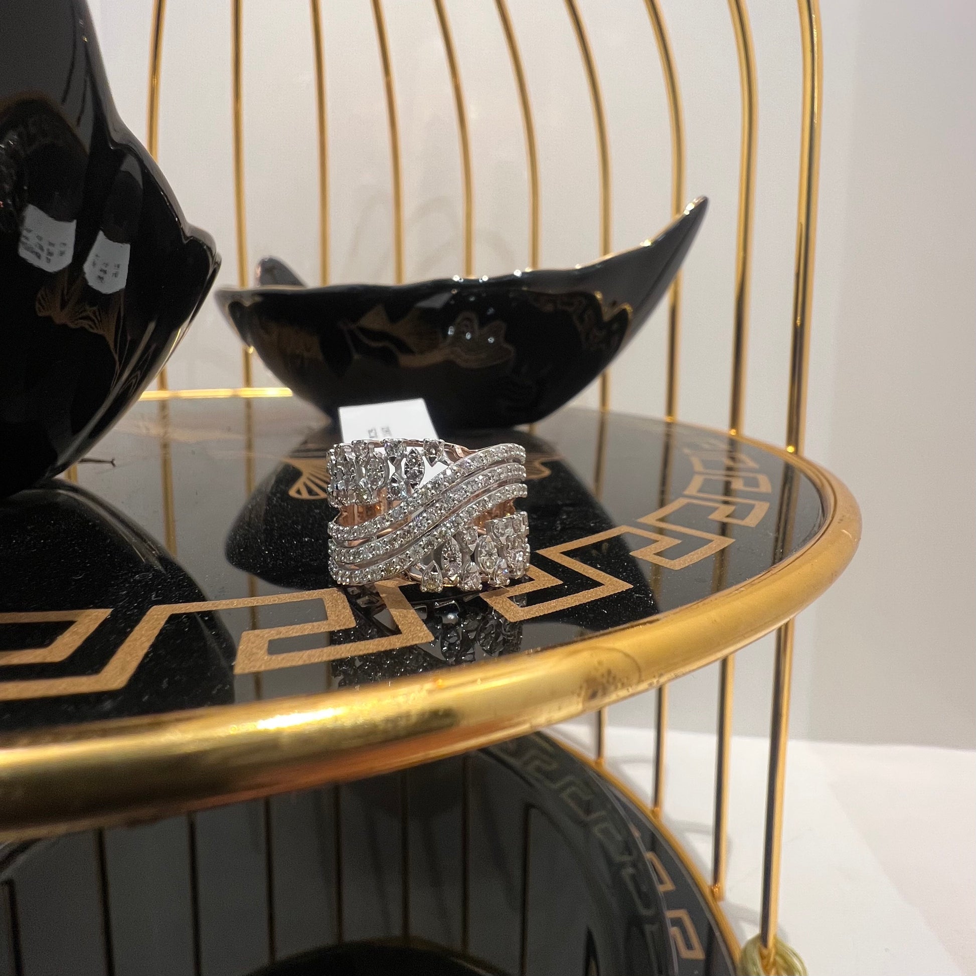 Close-up of an elegant wide diamond ring, featuring multiple crisscrossing bands adorned with round-cut diamonds set in gold, displayed on a black reflective surface.