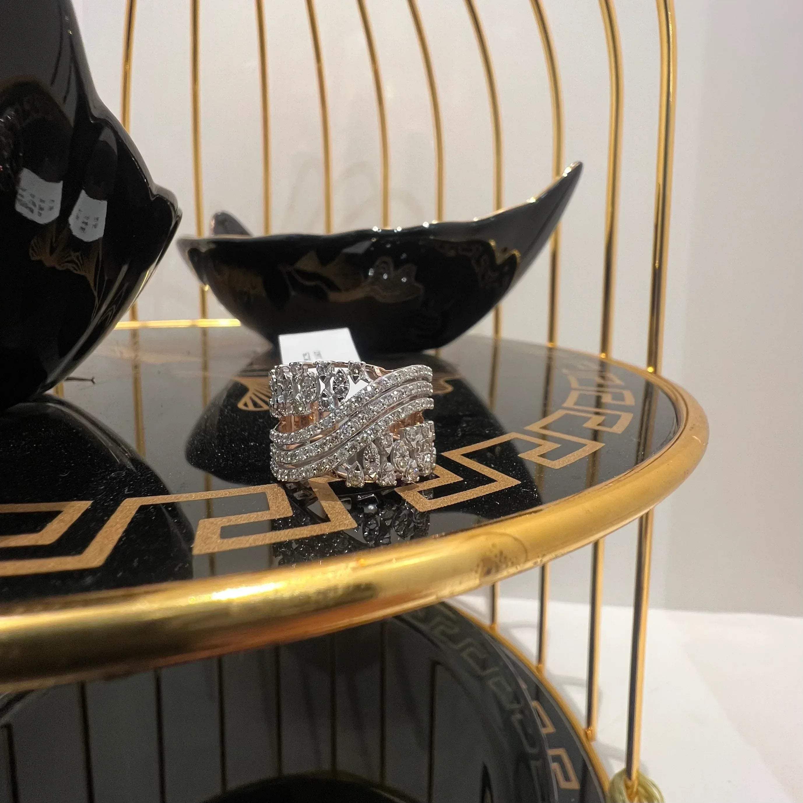 Close-up of an elegant wide diamond ring, featuring multiple crisscrossing bands adorned with round-cut diamonds set in gold, displayed on a black reflective surface.