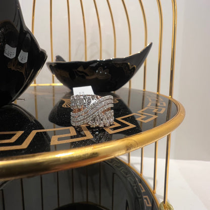 Close-up of an elegant wide diamond ring, featuring multiple crisscrossing bands adorned with round-cut diamonds set in gold, displayed on a black reflective surface.