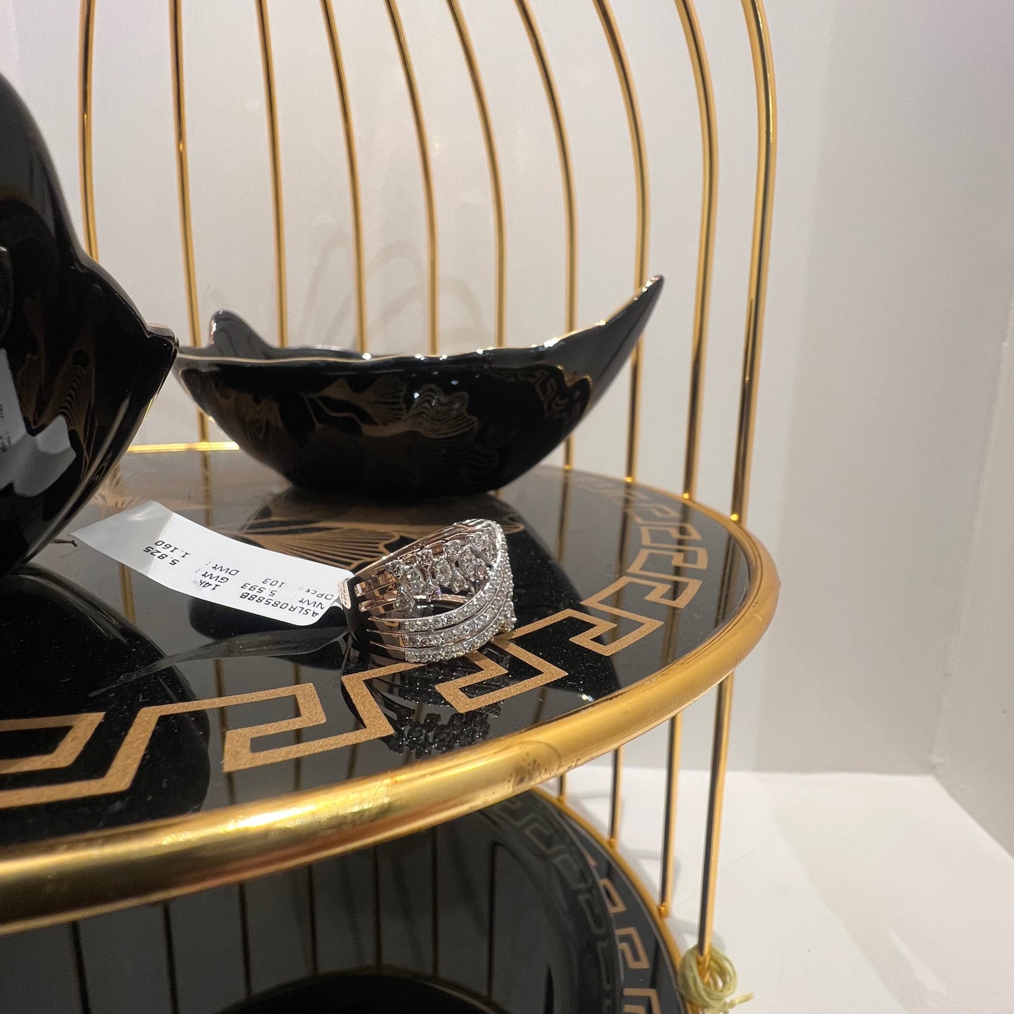 Close-up of an elegant wide diamond ring, featuring multiple crisscrossing bands adorned with round-cut diamonds set in gold, displayed on a black reflective surface.