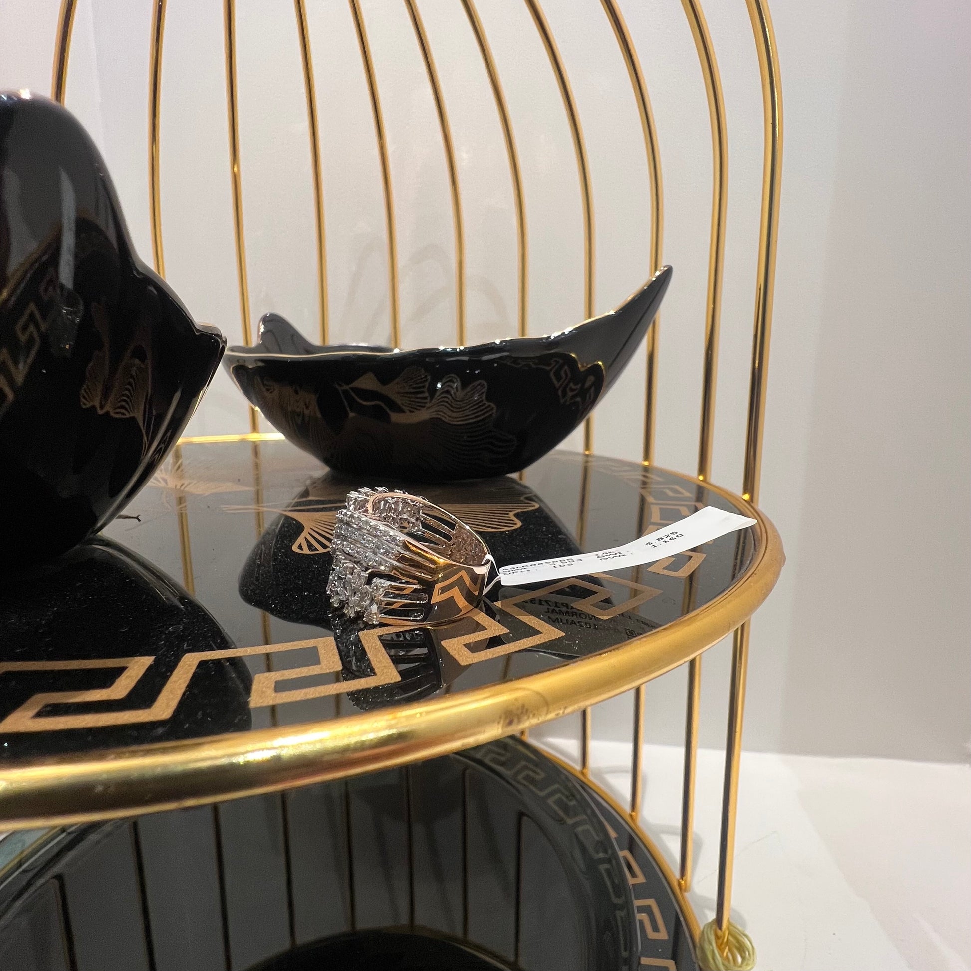 Close-up of an elegant wide diamond ring, featuring multiple crisscrossing bands adorned with round-cut diamonds set in gold, displayed on a black reflective surface.