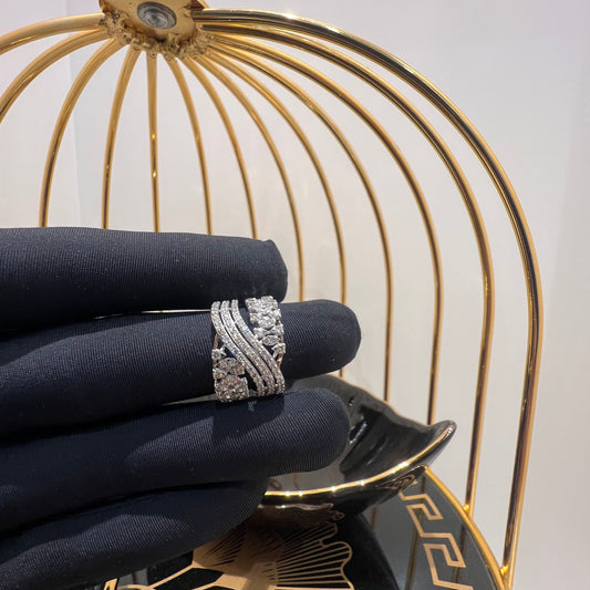 Close-up of an elegant wide diamond ring held by a gloved hand, featuring multiple crisscrossing bands adorned with round-cut diamonds set in gold, displayed against a gold decorative cage background.