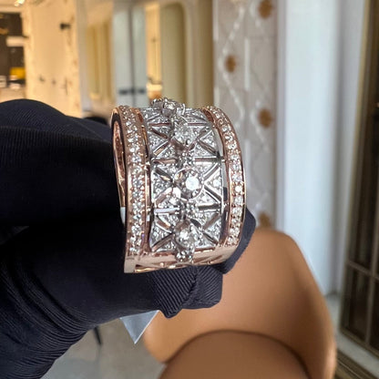 A ring with a band-style design, featuring a central diamond surrounded by smaller diamonds set in a gold band, held on a gloved hand.