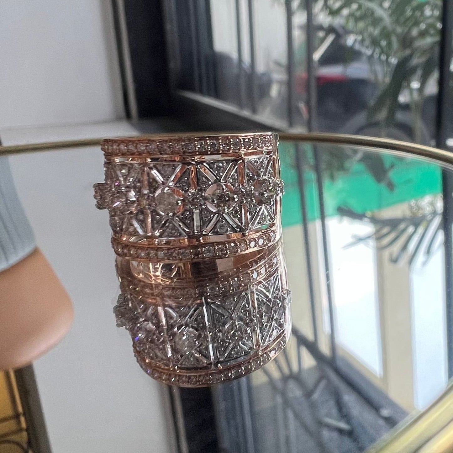 A ring with a band-style design, featuring a central diamond surrounded by smaller diamonds set in a gold band, displayed on a reflective surface.