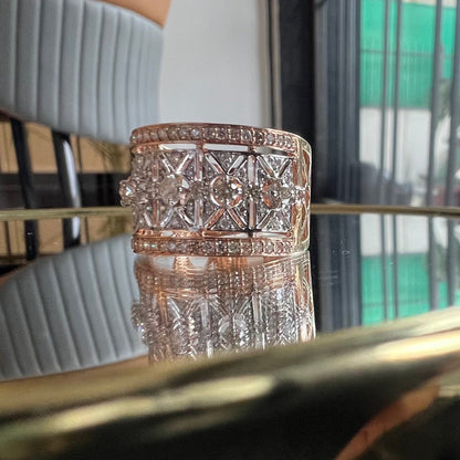 A ring with a band-style design, featuring a central diamond surrounded by smaller diamonds set in a gold band, displayed on a reflective surface.