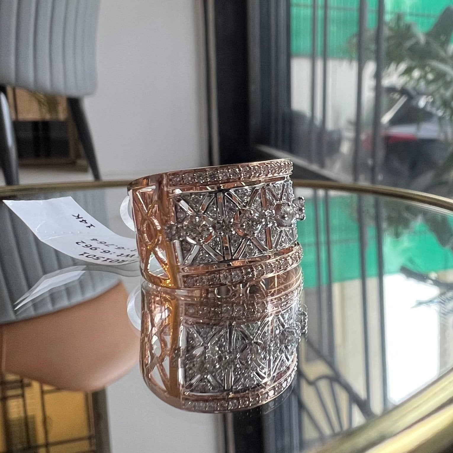 A ring with a band-style design, featuring a central diamond surrounded by smaller diamonds set in a gold band, displayed on a reflective surface.