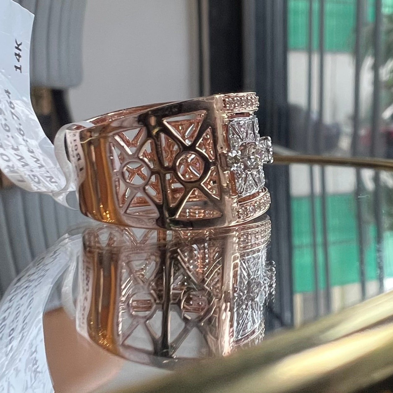 A ring with a band-style design, featuring a central diamond surrounded by smaller diamonds set in a gold band, displayed on a reflective surface.