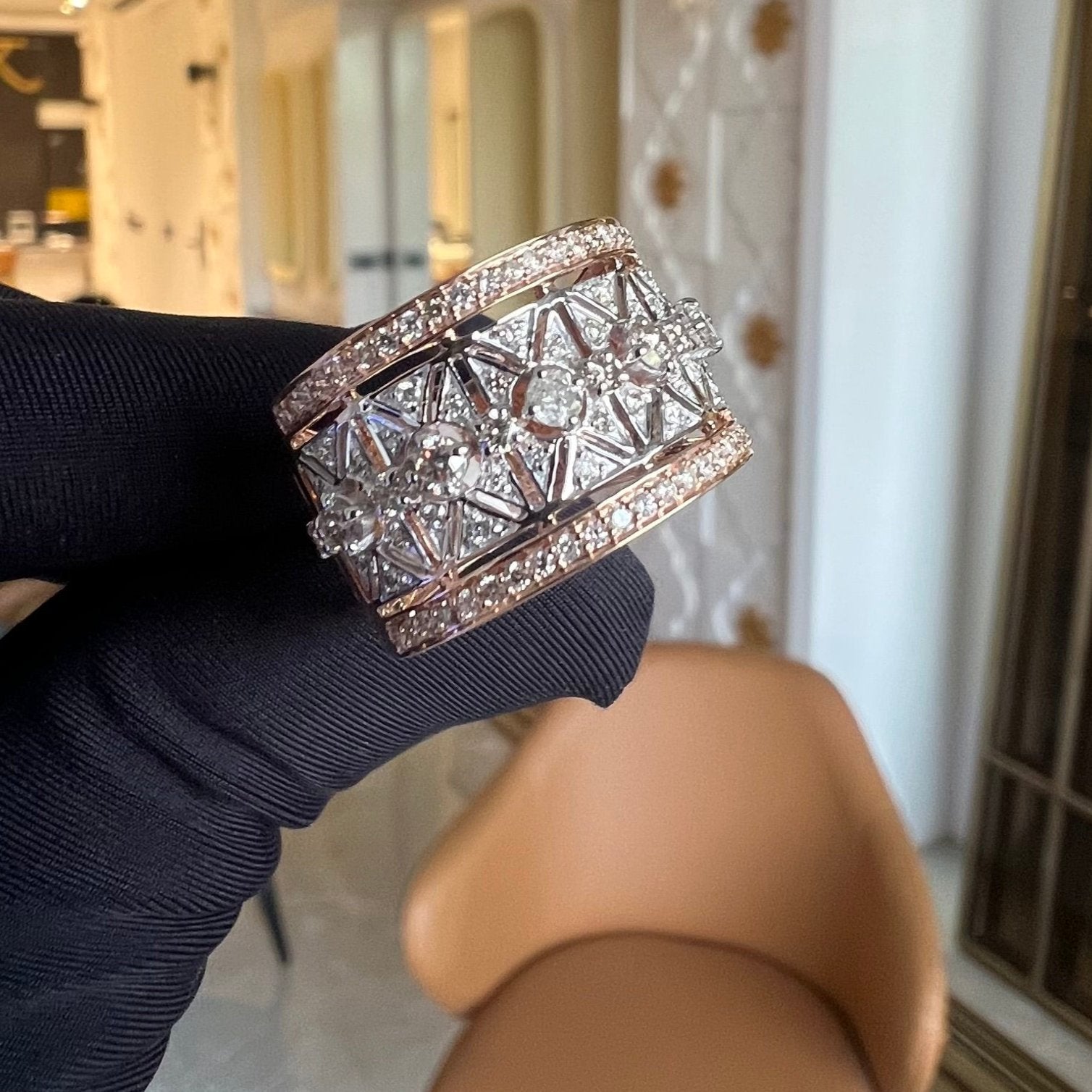 A ring with a band-style design, featuring a central diamond surrounded by smaller diamonds set in a gold band, displayed by a hand.