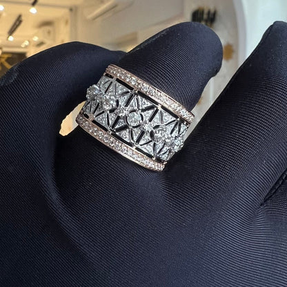 A ring with a band-style design, featuring a central diamond surrounded by smaller diamonds set in a gold band, held on a gloved hand.