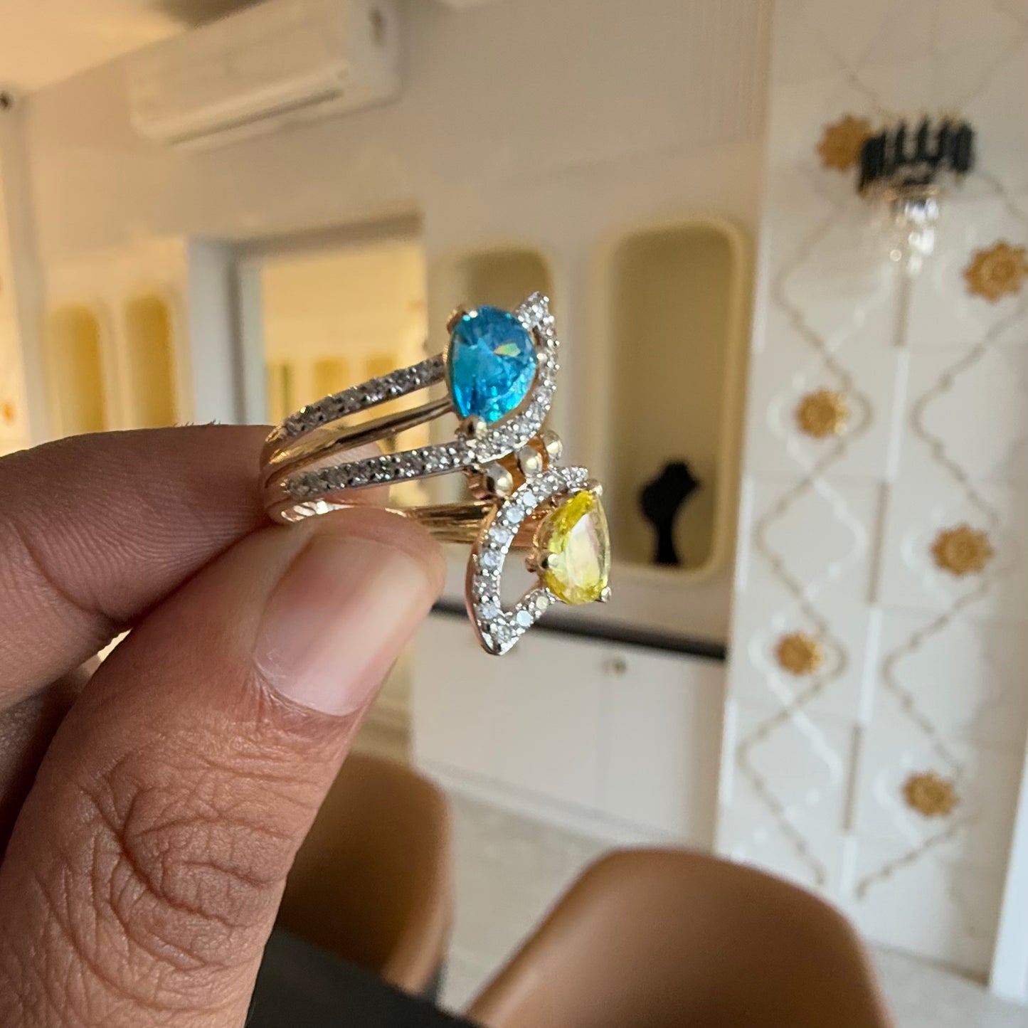A person's hand displaying a two-stone diamond ring with yellow and blue colors, made of 14kt gold.