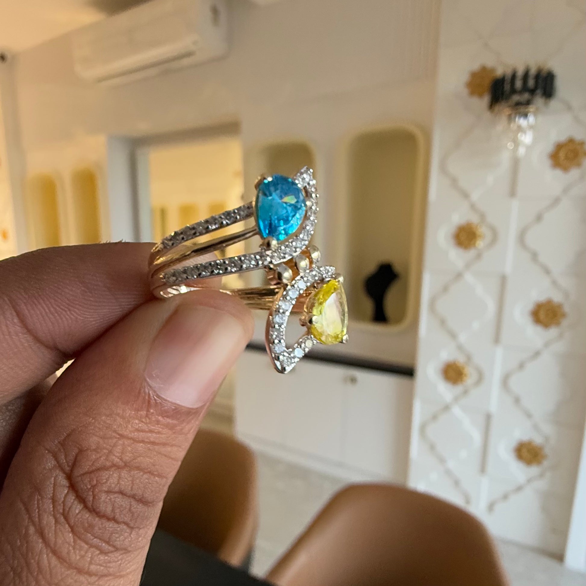 A person's hand displaying a two-stone diamond ring with yellow and blue colors, made of 14kt gold.