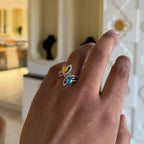 A person's hand displaying a two-stone diamond ring with yellow and blue colors, made of 14kt gold.