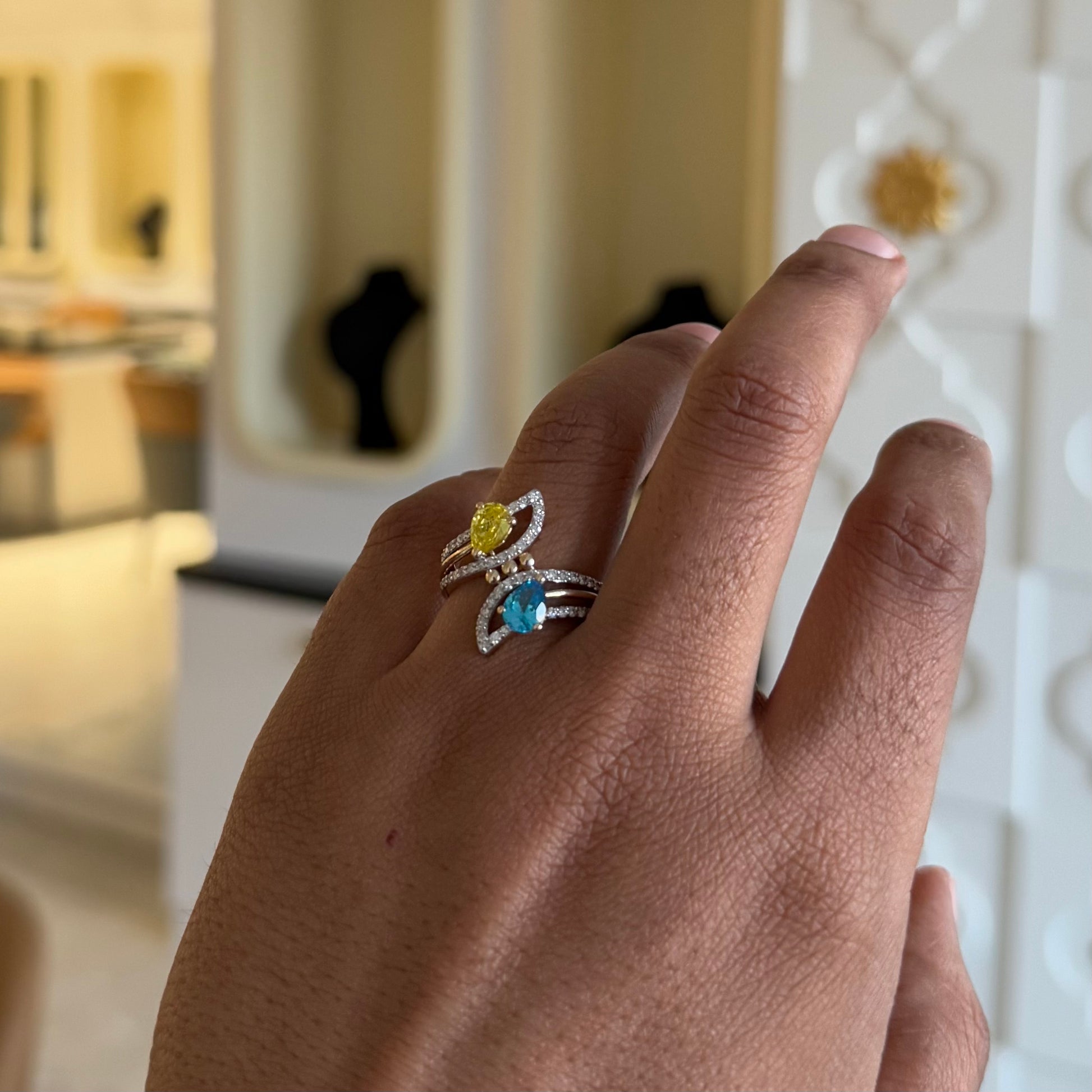 A person's hand displaying a two-stone diamond ring with yellow and blue colors, made of 14kt gold.