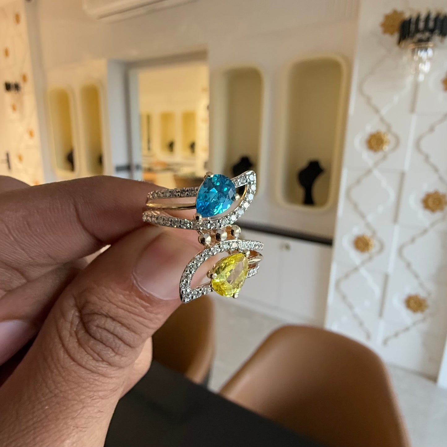 A person's hand displaying a two-stone diamond ring with yellow and blue colors, made of 14kt gold.
