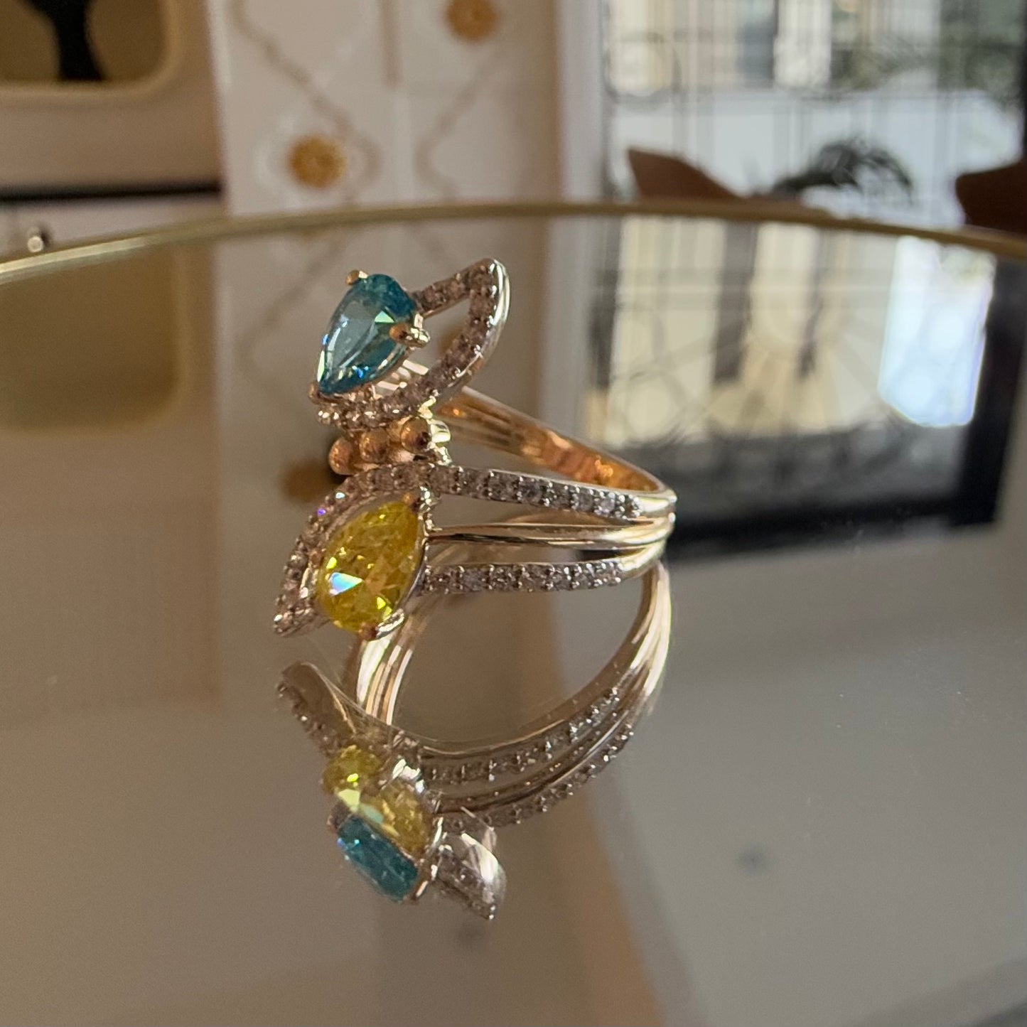 A reflective table displaying a two-stone diamond ring with yellow and blue colors, made of 14kt gold.