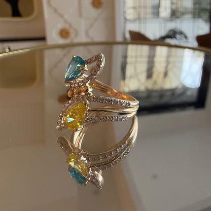 A reflective table displaying a two-stone diamond ring with yellow and blue colors, made of 14kt gold.