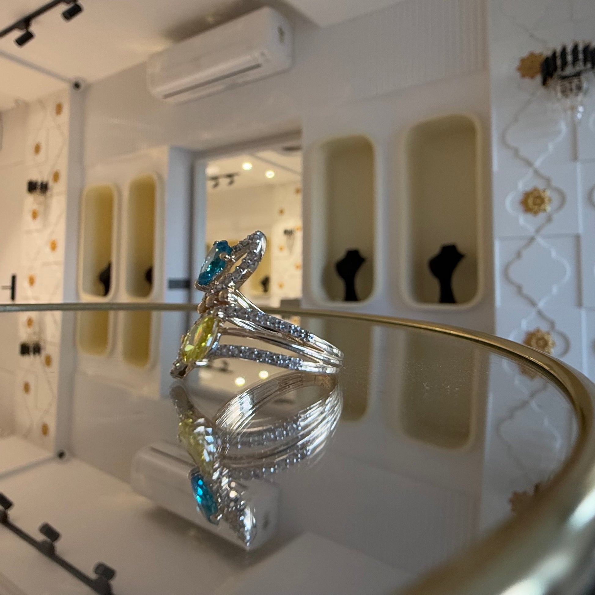 A reflective table displaying a two-stone diamond ring with yellow and blue colors, made of 14kt gold.