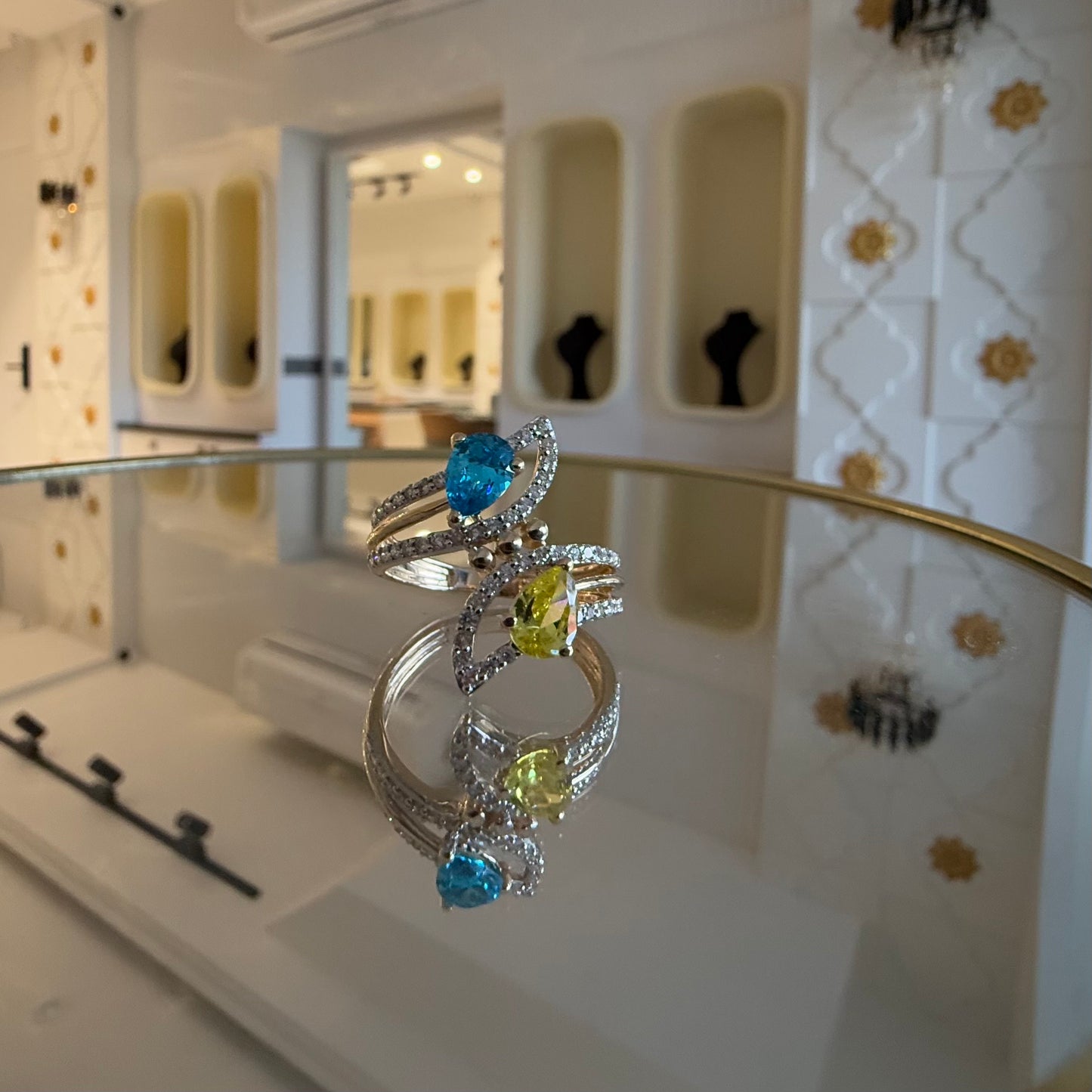 A reflective table displaying a two-stone diamond ring with yellow and blue colors, made of 14kt gold.