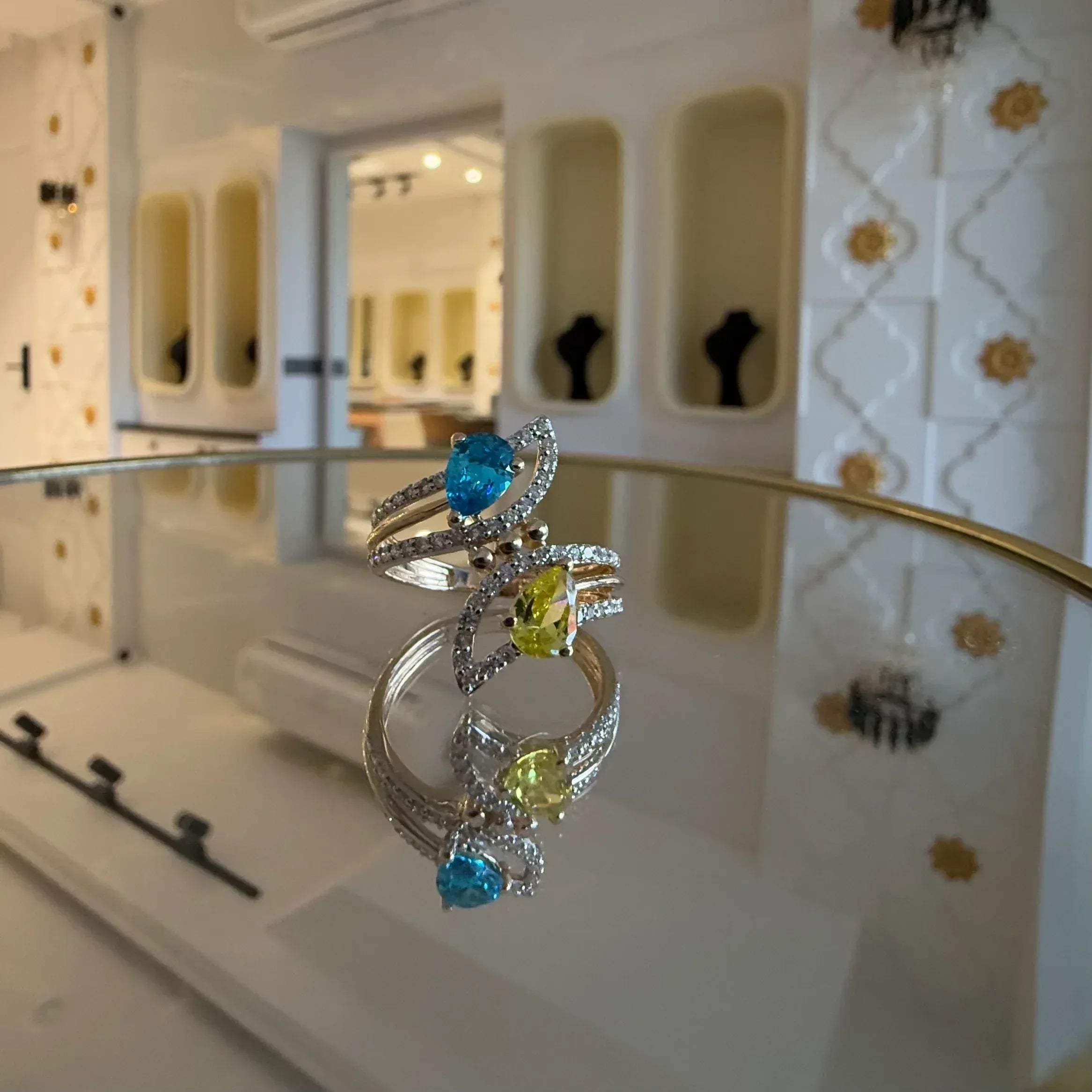A reflective table displaying a two-stone diamond ring with yellow and blue colors, made of 14kt gold.
