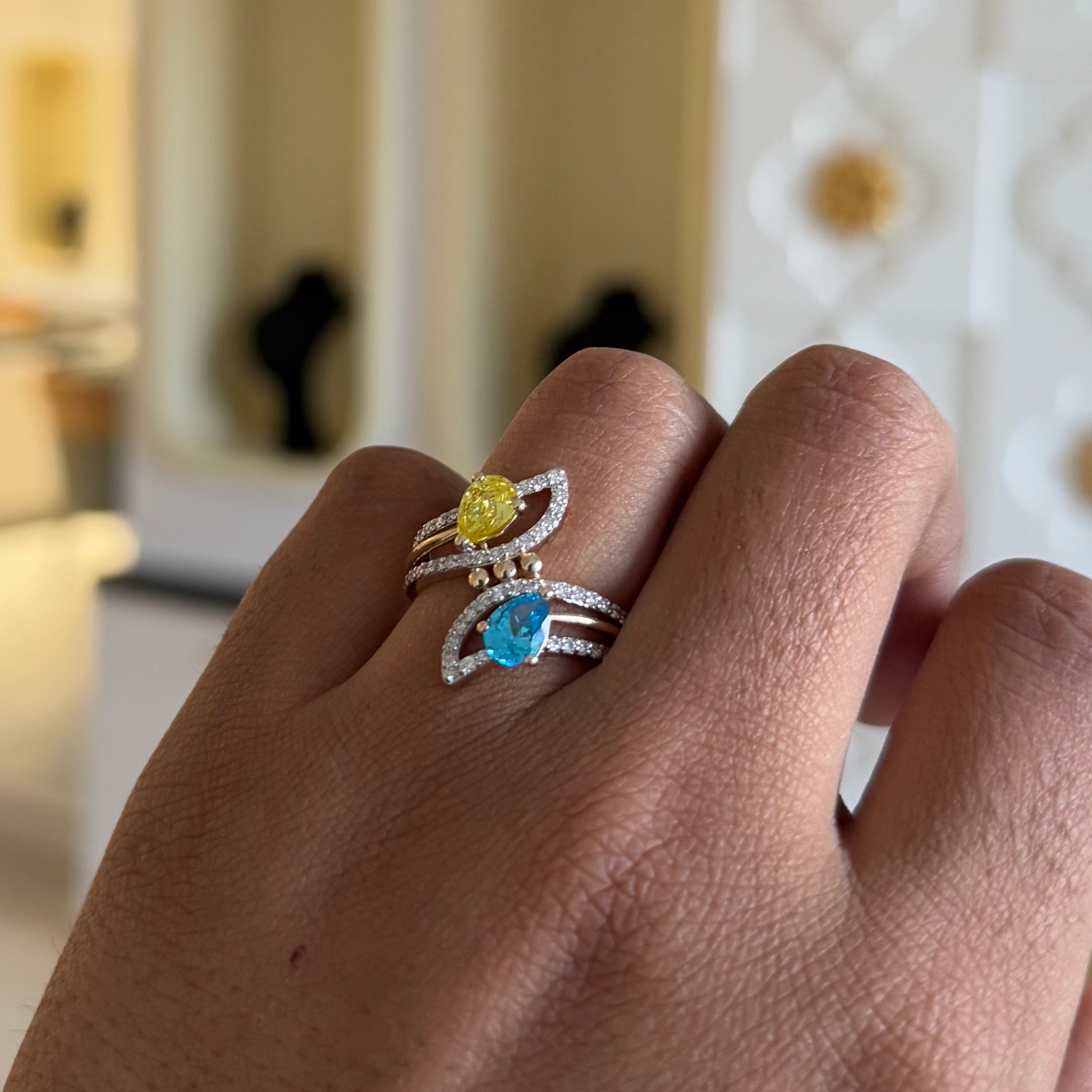 A person's hand displaying a two-stone diamond ring with yellow and blue colors, made of 14kt gold.