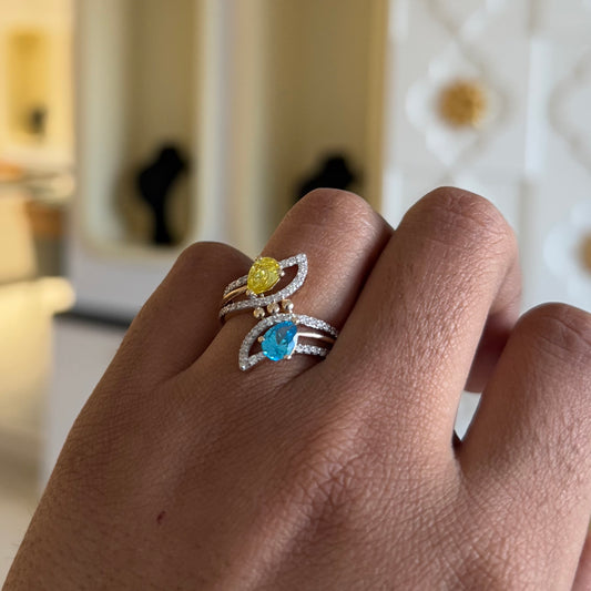 A person's hand displaying a two-stone diamond ring with yellow and blue colors, made of 14kt gold.
