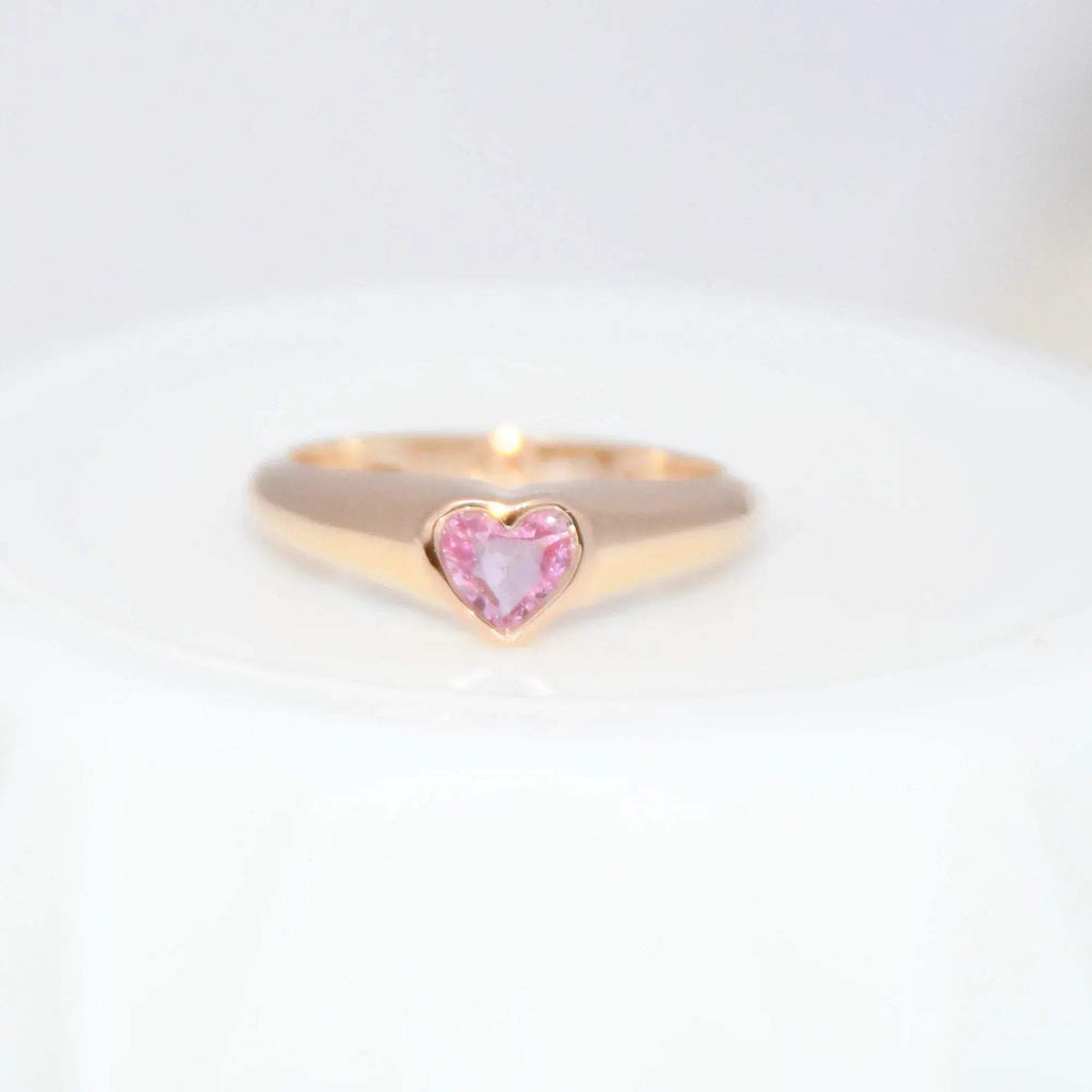 Gold ring with a heart-shaped pink sapphire gemstone on a white background.