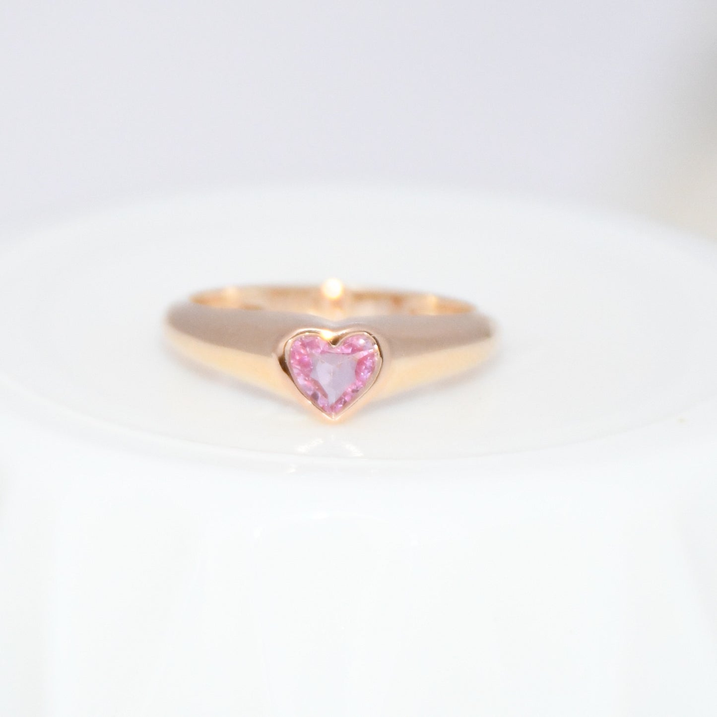 Gold ring with a heart-shaped pink sapphire gemstone on a white background.