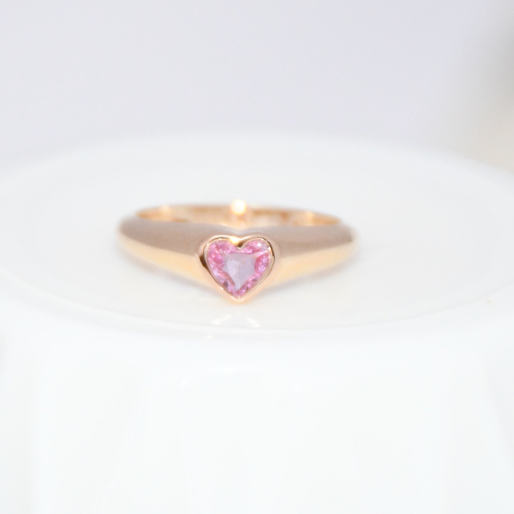 Gold ring with a heart-shaped pink sapphire gemstone on a white background.