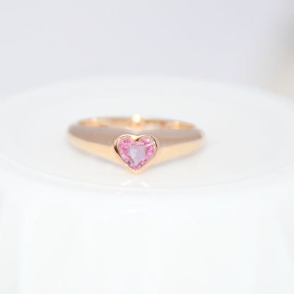Gold ring with a heart-shaped pink sapphire gemstone on a white background.