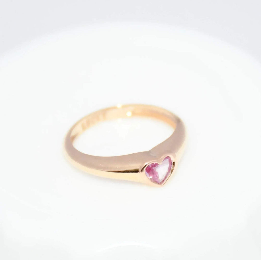 Gold ring with a heart-shaped pink sapphire gemstone on a white background