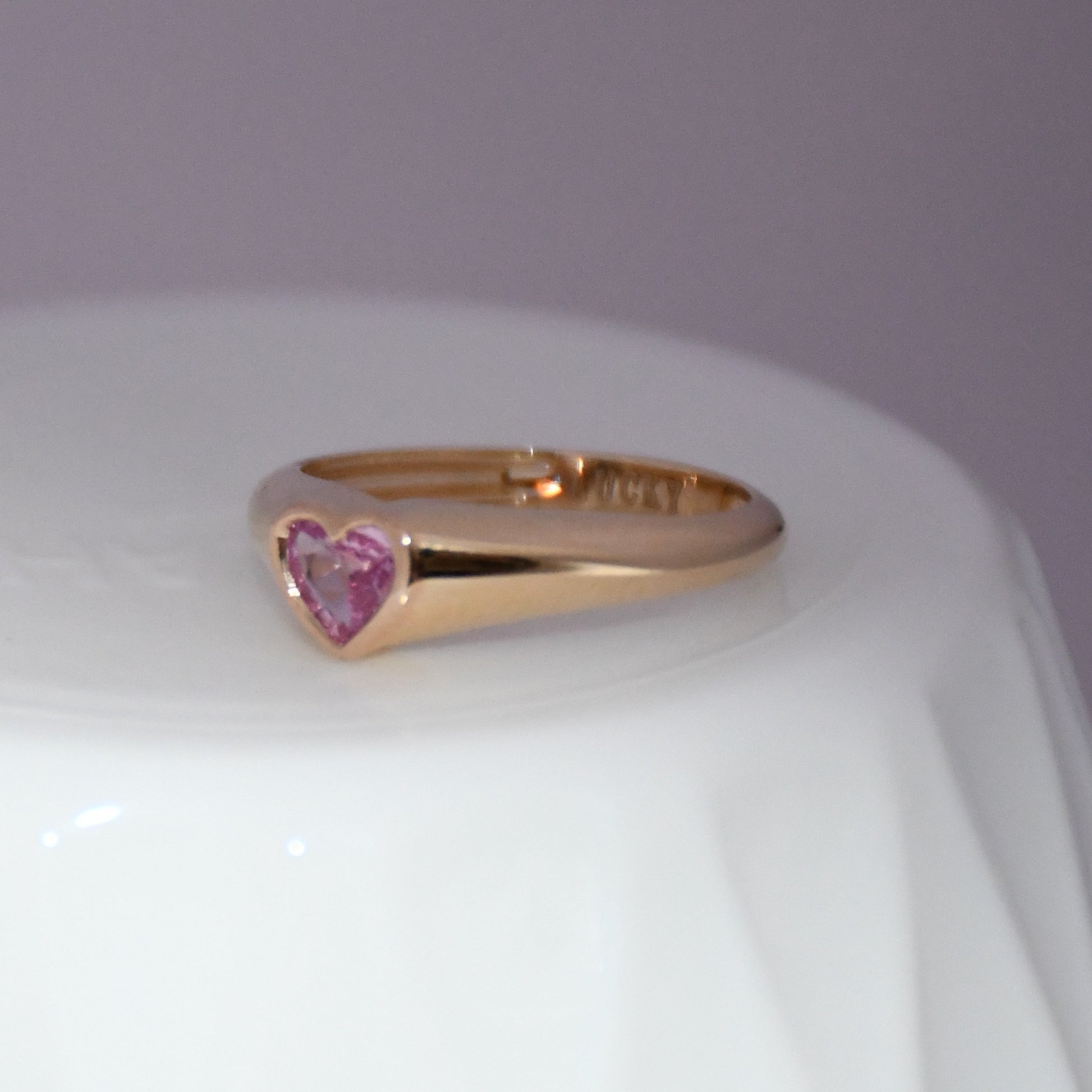 Gold ring with a heart-shaped pink sapphire gemstone on a white background