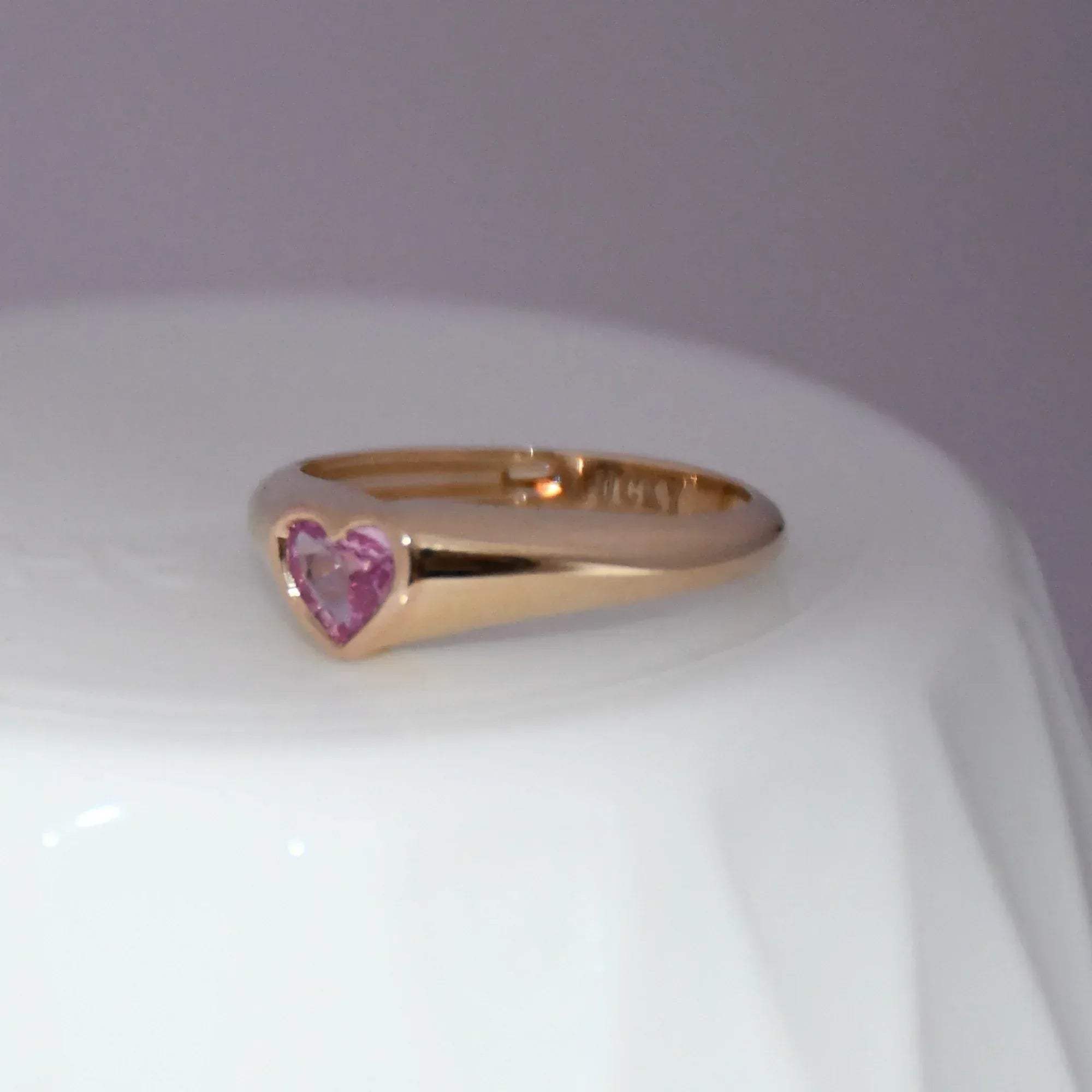 Gold ring with a heart-shaped pink sapphire gemstone on a white background