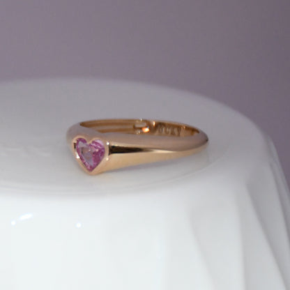 Gold ring with a heart-shaped pink sapphire gemstone on a white background