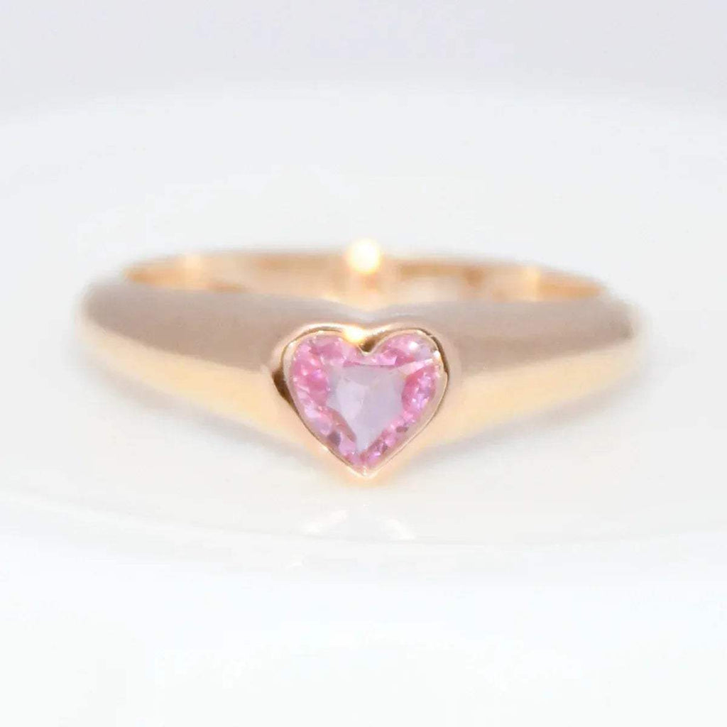 Gold ring with a heart-shaped pink sapphire gemstone on a white background