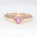 Gold ring with a heart-shaped pink sapphire gemstone on a white background