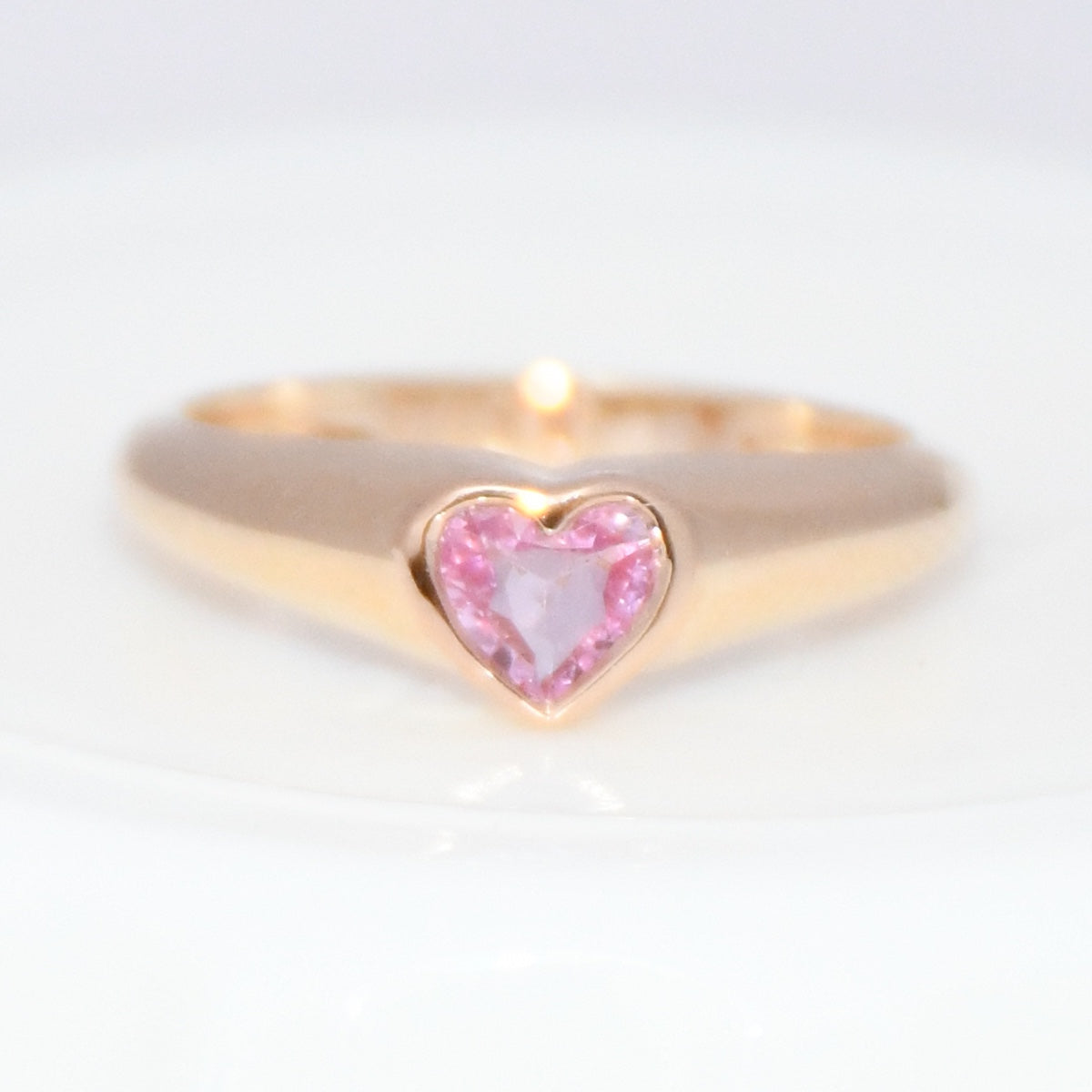 Gold ring with a heart-shaped pink sapphire gemstone on a white background