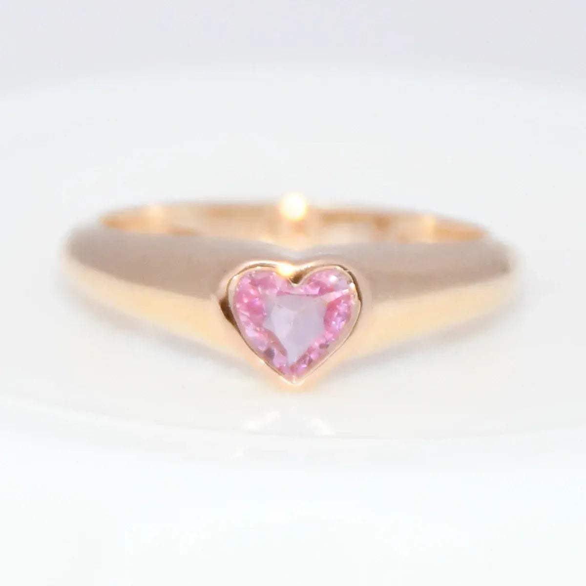 Gold ring with a heart-shaped pink sapphire gemstone on a white background