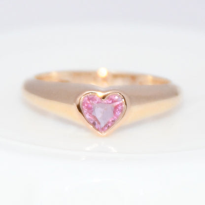 Gold ring with a heart-shaped pink sapphire gemstone on a white background